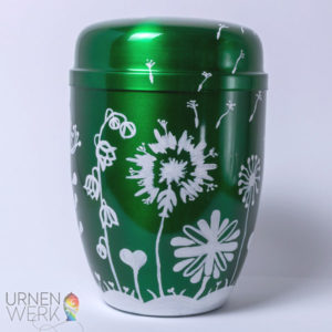 Verschiedene weisse Blumen zieren diese dunkelgruene Metall Urne